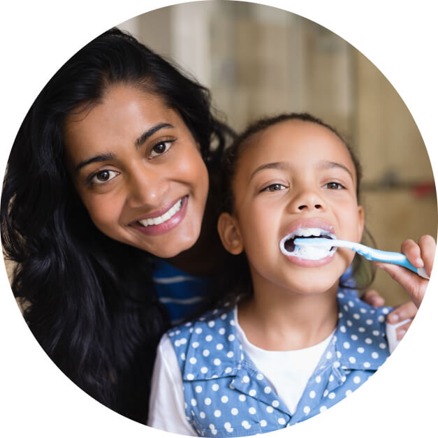 Mother helping her young daughter brush her teeth